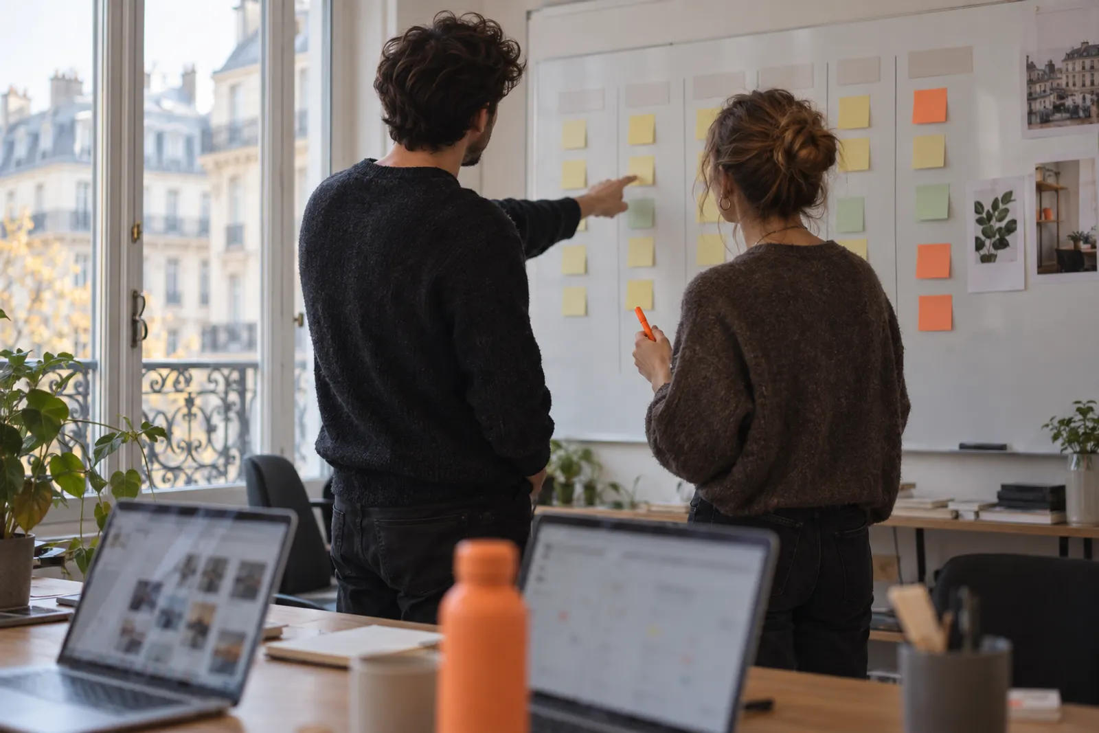 Deux membres d’une agence organisent un plan de contenus devant un tableau couvert de notes.