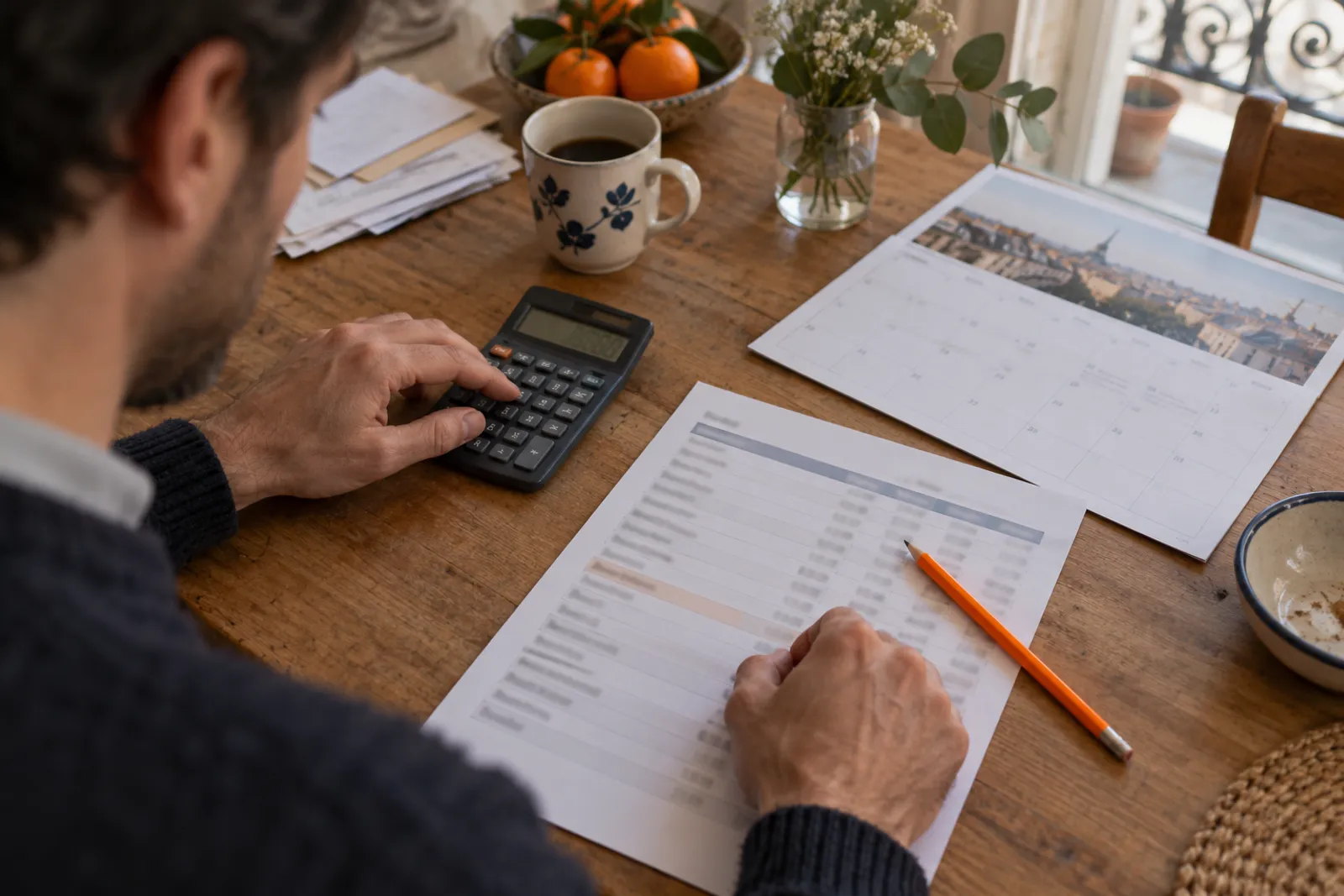 Des mains font un calcul de budget mensuel avec une calculatrice et un calendrier papier.