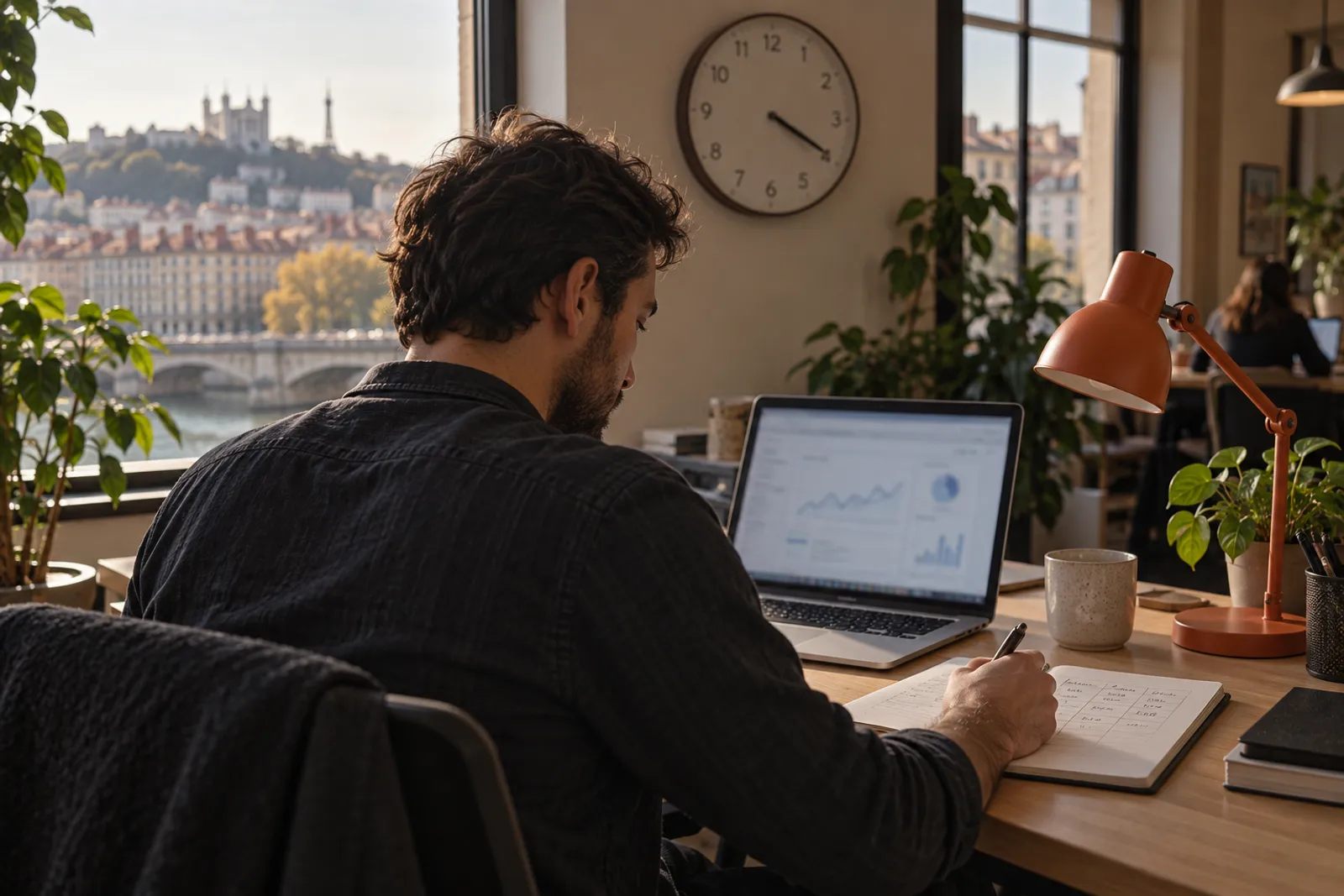 Un consultant note ses heures de travail dans un carnet, à côté de son ordinateur, dans un espace de coworking.